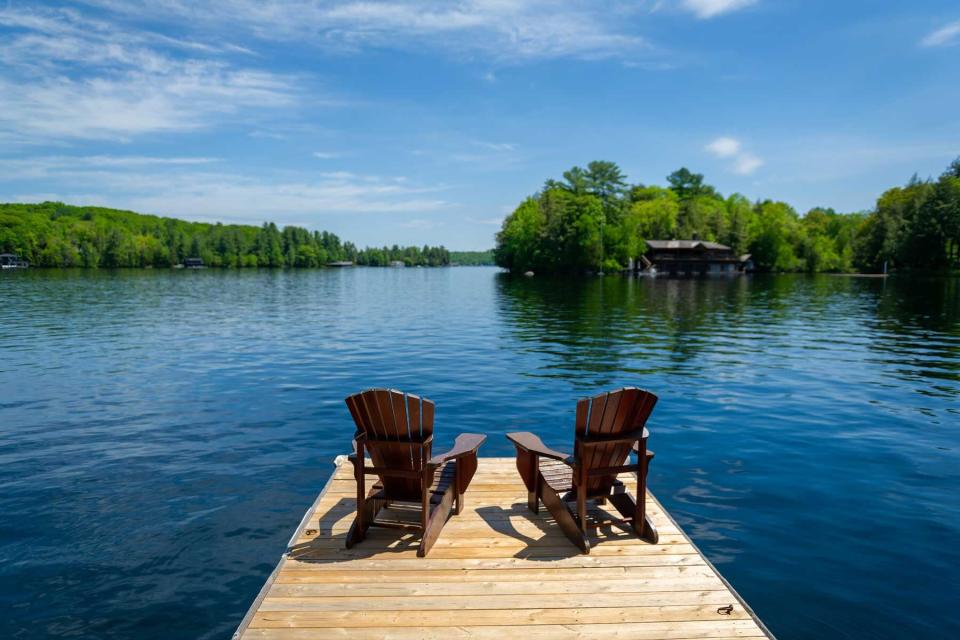 Empty Adirondack chairs sitting on a dock by a lake