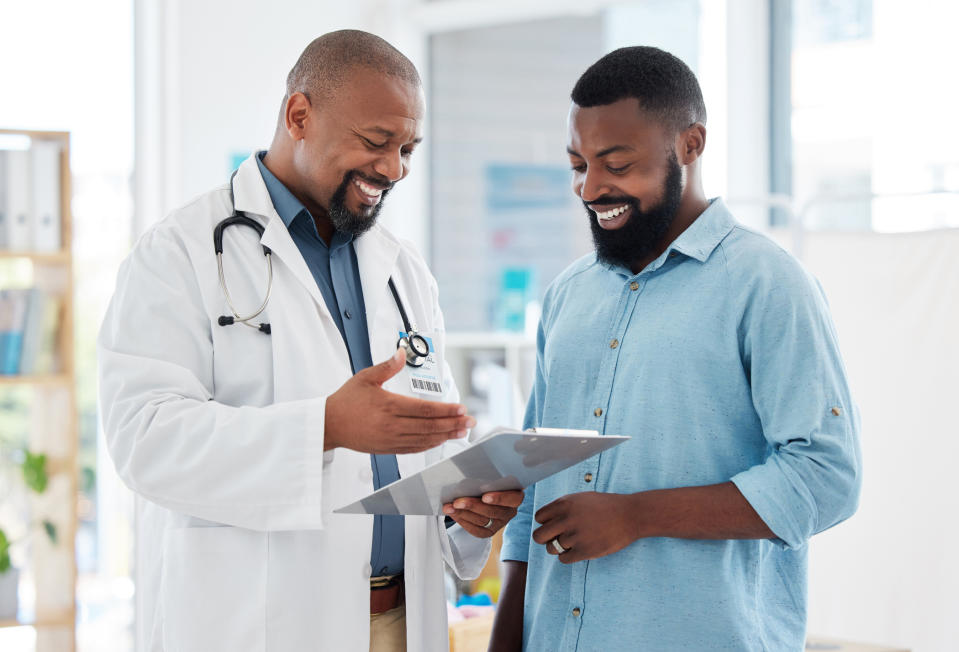 A doctor in a white coat shows a patient in a casual shirt a document, both smiling and discussing the contents, in a professional medical setting