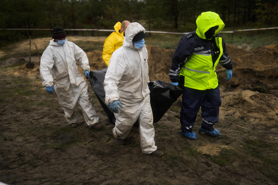 Members of a forensic team carry a plastic bag with a body inside as they work at an exhumation in a mass grave in Lyman, Ukraine, Tuesday, Oct. 11, 2022. (AP Photo/Francisco Seco)