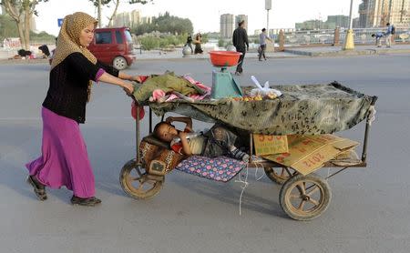 An ethnic Uighur woman pushes her fruit stall while her child lies in it along a street in Asku, Xinjiang Uighur Autonomous Region in this June 14, 2012 file photo. REUTERS/Stringer/Files