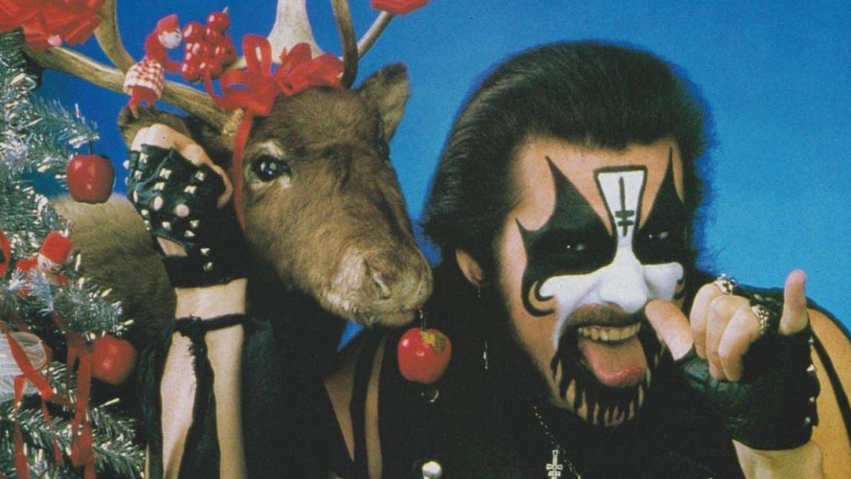  King Diamond posing next to a reindeer that has tinsel on its head. 