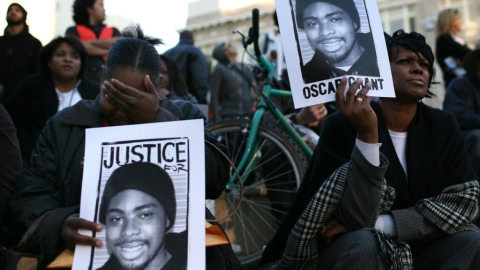 This January 2009 photo shows protesters with signs picturing slain 22-year-old Oscar Grant III, who was shot in the back by a Bay Area Rapid Transit police officer as he lay face down on the ground, during a demonstration at Oakland City Hall. (Photo by Justin Sullivan/Getty Images)