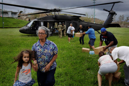 A woman and child walk away as soldiers in a UH-60 Blackhawk helicopter from the First Armored Division's Combat Aviation Brigade deliver food and water during recovery efforts following Hurricane Maria in Verde de Comerio, Puerto Rico, October 7, 2017. REUTERS/Lucas Jackson