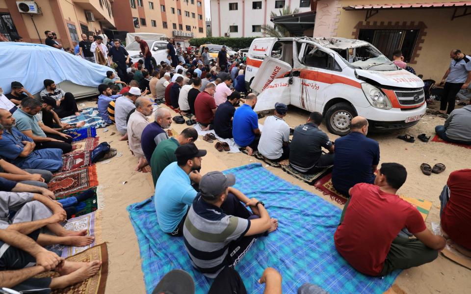 Palestinian men, seated on the ground close to a damaged ambulance, take part in Friday Noon prayers in the drive way of the emergency entrance of the Nasser hospital in Khan Yunis