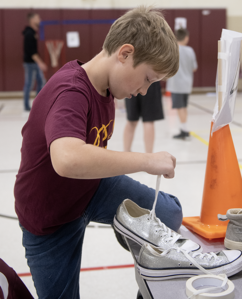 To simulate a fine motor impairment, Lucas Moore, 10, ties a shoe with one arm during Southeast intermediate and primary schools' Abilities Week.