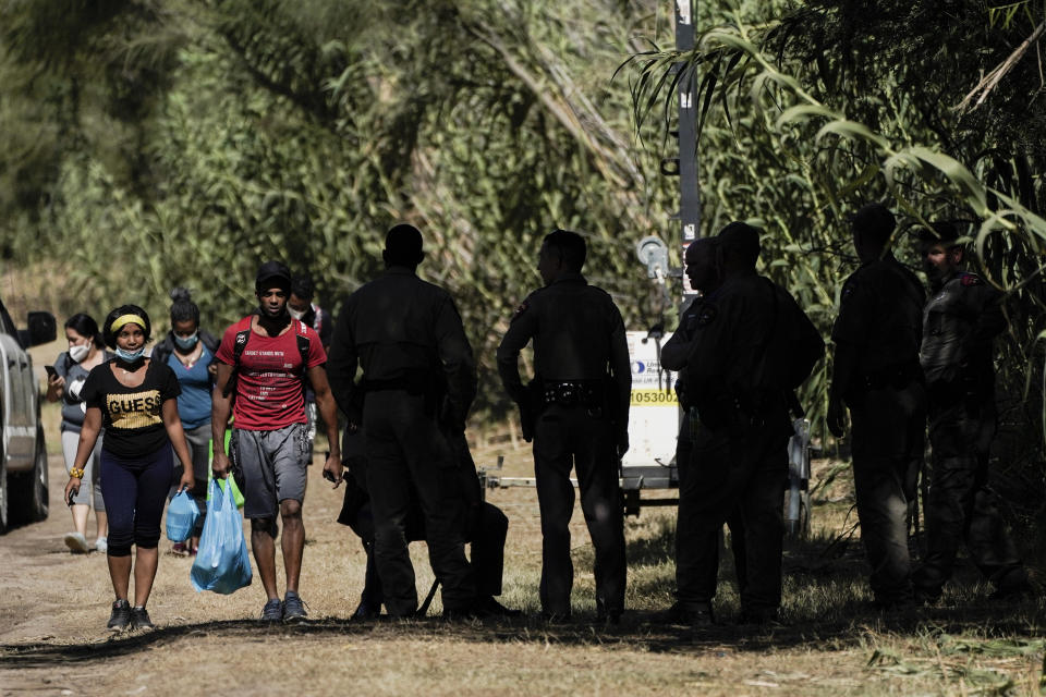 Cuban nationals, left, walk near Texas Department of Public Safety officials, right, on a road along the Rio Grande after crossing the river while seeking asylum, Thursday, Sept. 23, 2021, in Del Rio, Texas.The “amistad,” or friendship, that Del Rio, Texas, and Ciudad Acuña, Mexico, celebrate with a festival each year has been important in helping them deal with the challenges from a migrant camp that shut down the border bridge between the two communities for more than a week. Federal officials announced the border crossing would reopen to passenger traffic late Saturday afternoon and to cargo traffic on Monday. (AP Photo/Julio Cortez)