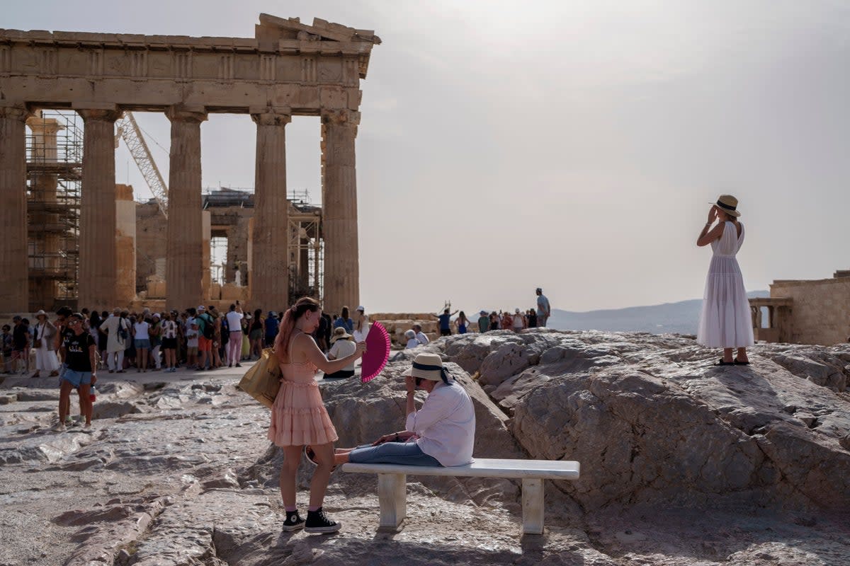 A tourist uses a hand fan to cool down another one sitting on a bench in front of the Parthenon at the ancient Acropolis, in Athens (AP)