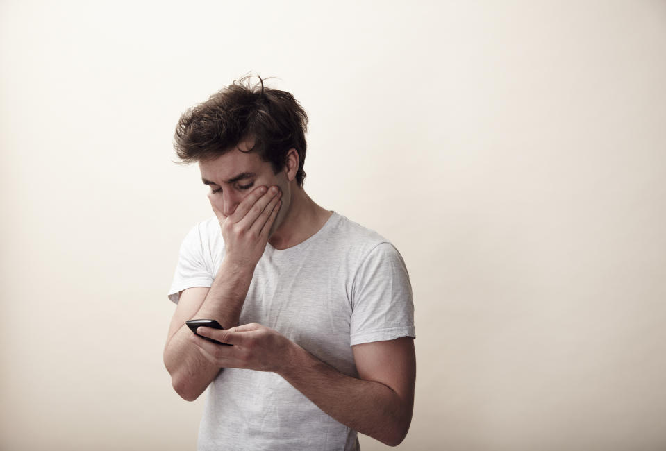 Man in a white tee looking at phone with a distressed expression, possibly relating to a personal issue