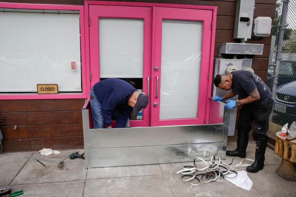 Angelo Coric and Feliciano Cinta, right install a metal flood gate in front of Pink Onion, a pizzeria in the Mission District in San Francisco, on Tuesday in preparation of storms. Pink Onion saw serious flooding and damage on Saturday in the wake of a storm (AP)