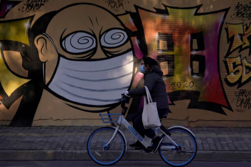 A woman wearing a protective mask cycles past graffiti-painted wall in Shanghai