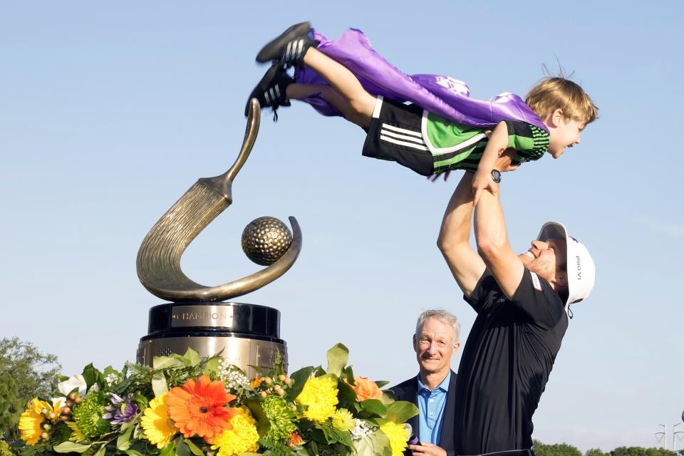 Peter Malnati, right, holds up his son Hatcher after winning the Valspar Championship golf tournament Sunday, March 24, 2024, at Innisbrook in Palm Harbor, Fla. Looking on is emcee Gary Koch. (AP Photo/Chris O'Meara)