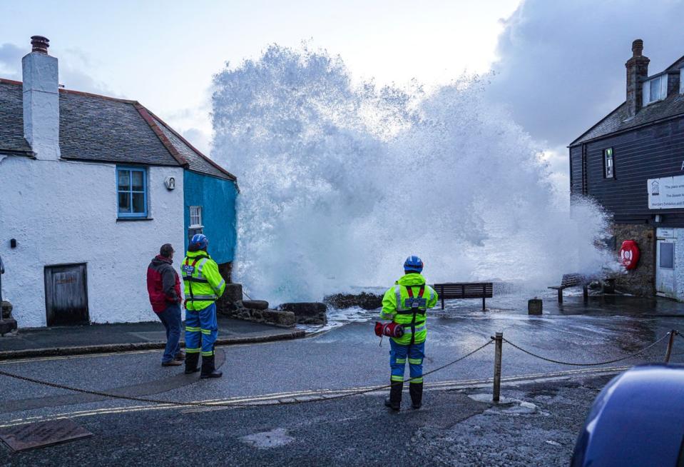 HM Coastguard personnel look on as waves crash over the harbour wall onto the street in St Ives (Getty Images)