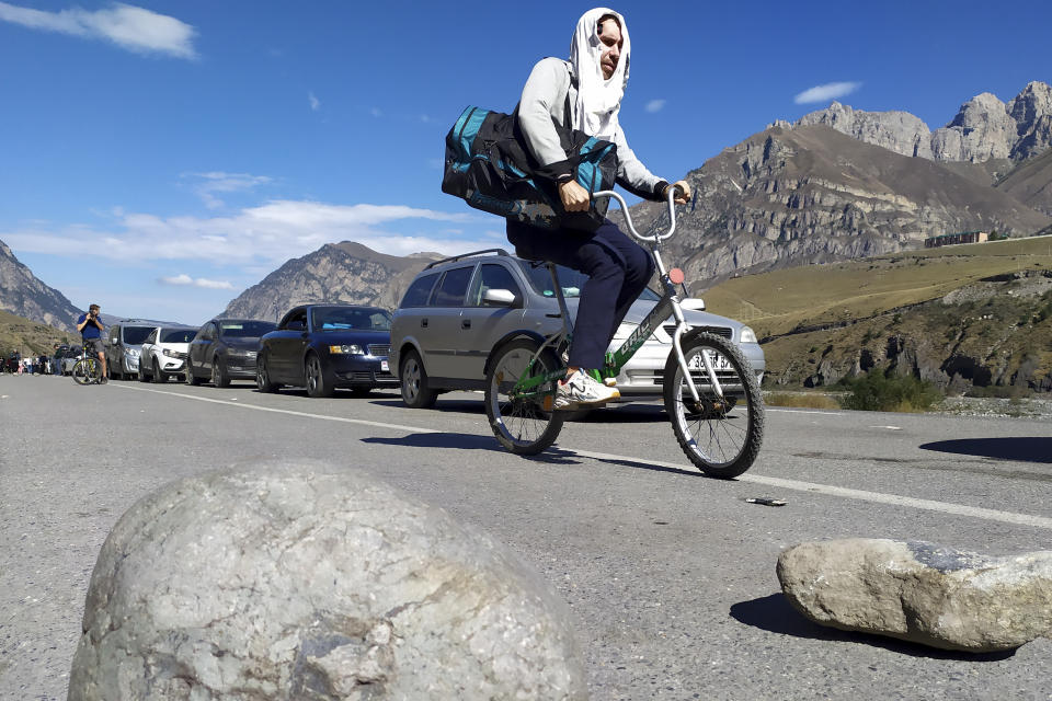 A Russian man rides a bicycle towards the border crossing at Verkhny Lars between Georgia and Russia leaving Chmi, North Ossetia - Alania Republic, Russia, Thursday, Sept. 29, 2022. Long lines of vehicles have formed at a border crossing between Russia's North Ossetia region and Georgia after Moscow announced a partial military mobilization. A day after President Vladimir Putin ordered a partial mobilization to bolster his troops in Ukraine, many Russians are leaving their homes. (AP Photo)