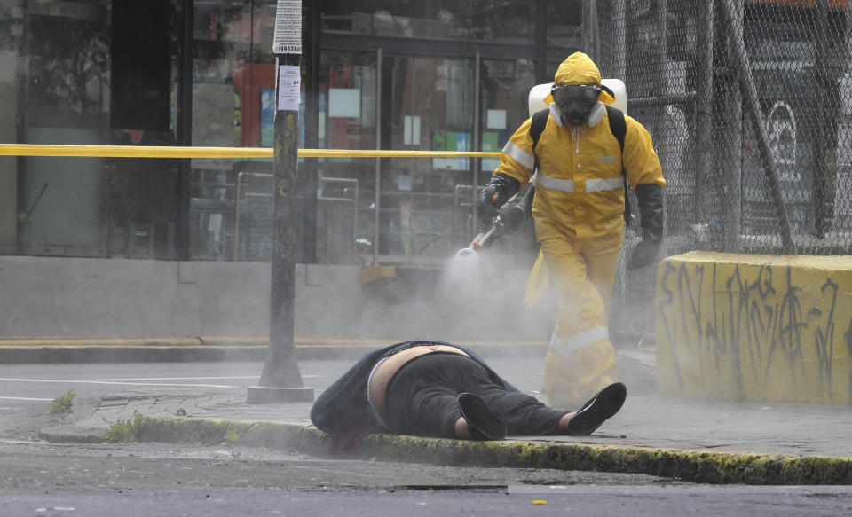 A city forensic worker sprays disinfectant on the body of a woman who died in the street in Quito, Ecuador, Thursday, May 14, 2020. Forensics conducted a COVID-19 rapid test and said the woman tested negative. (AP Photo/Dolores Ochoa)