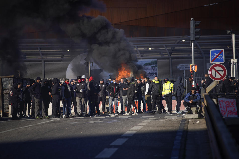 Dock workers stand in front of a burning barricade next the port of Marseille southern France, Wednesday, March 22, 2023.The bill pushed through by President Emmanuel Macron without lawmakers' approval still faces a review by the Constitutional Council before it can be signed into law. Meanwhile, oil shipments in the country were disrupted amid strikes at several refineries in western and southern France. (AP Photo/Daniel Cole)