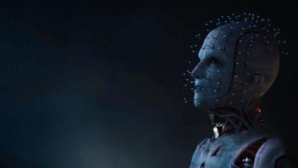 A still from Hulu's Hellraiser movie shows Jamie Clayton as The Priest, a white figure with jeweled pins coming out of her face