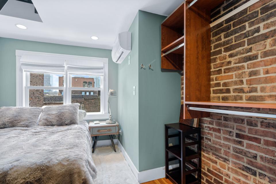 A bedroom with blue walls, exposed brick on the left and two windows in the back