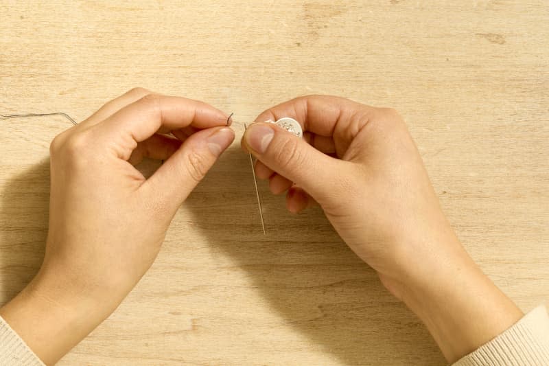 Overhead shot of two hands using a needle threader to thread a needle.