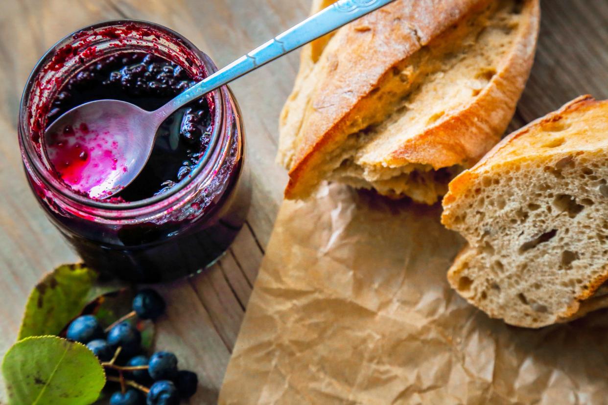 spoon in jar of chokeberry jam, fresh berries and bread