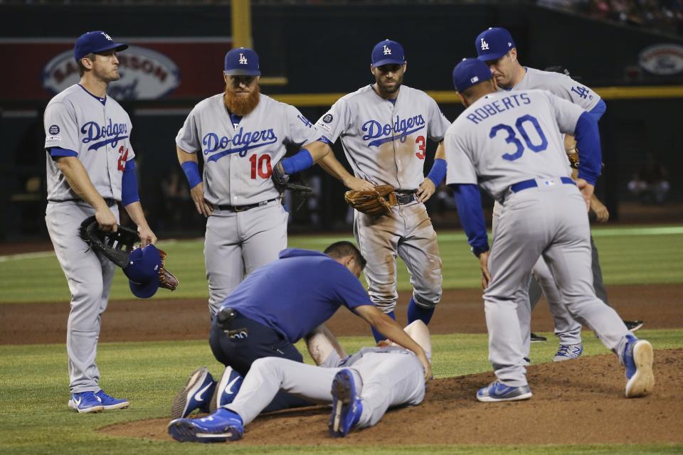 Los Angeles Dodgers medical staff Yosuke Nakajima, bottom left, attends to relief pitcher Dustin May, front, after May was hit by a batted ball from Arizona Diamondbacks' Jake Lamb during the fourth inning of a baseball game Sunday, Sept. 1, 2019, in Phoenix. Dodgers' David Freese, left, Justin Turner (10), Chris Taylor (3), Dave Roberts (30) and Jedd Gyorko, right, all look on. (AP Photo/Ross D. Franklin)