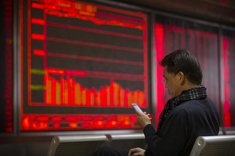 In this Tuesday, Nov. 19, 2019 photo, a Chinese investor uses a smartphone as he monitor stock prices at a brokerage house in Beijing. Shares retreated in Asia on Wednesday after Japan reported its worst monthly decline in exports in three years. (AP Photo/Mark Schiefelbein)