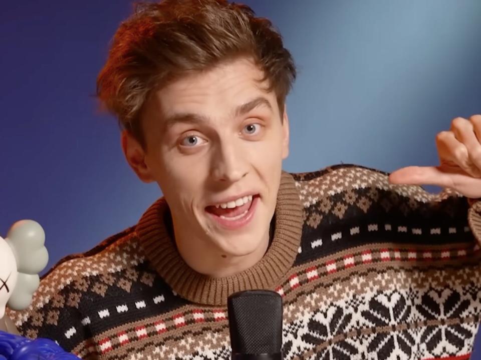 Screenshot of a recent A4 YouTube video, wearing a brown sweater and sitting in front of a microphone.