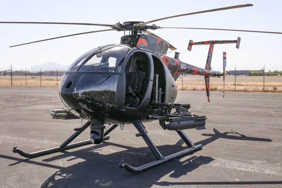 An MD Helicopters MD 530F-series light armed helicopter in a promotional paint job that includes a red/orange, gray, and black camouflage scheme on the doghouse and tail boom. <em>MD Helicopters</em>