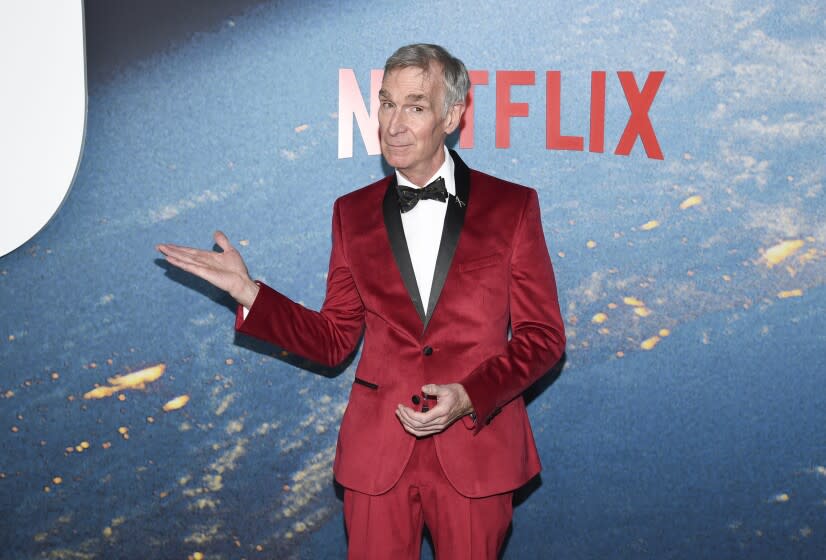 A man in a bright red velvet tuxedo gestures with one arm upon arrival at an event