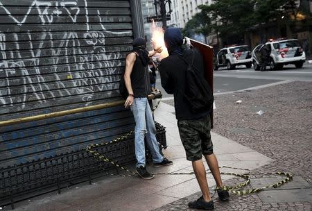 A demonstrator (L) sets off a flare bomb against riot police during a protest against fare hikes for city buses in Sao Paulo, Brazil, January 8, 2016. REUTERS/Nacho Doce
