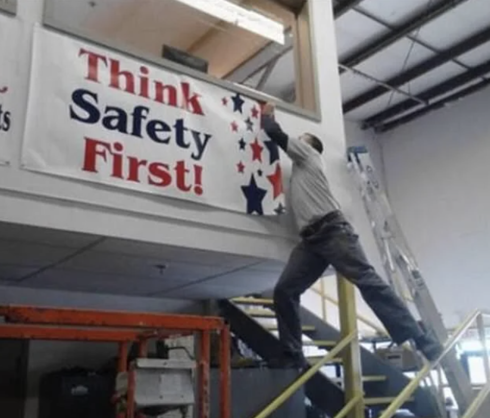 Person on top of a ladder reaching towards a "Think Safety First!" sign, unsafely balanced