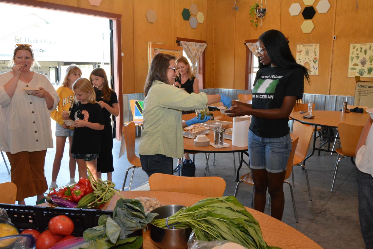 Bolupe Ogunyooye, right, receives a sampling Monday of vegetables grown the world over from Beth Teska with Columbia Center for Urban Agriculture during a Catholic Charities Refugee Services Welcome Week event at the MU Health Care Pavilion in Clary-Shy Park.