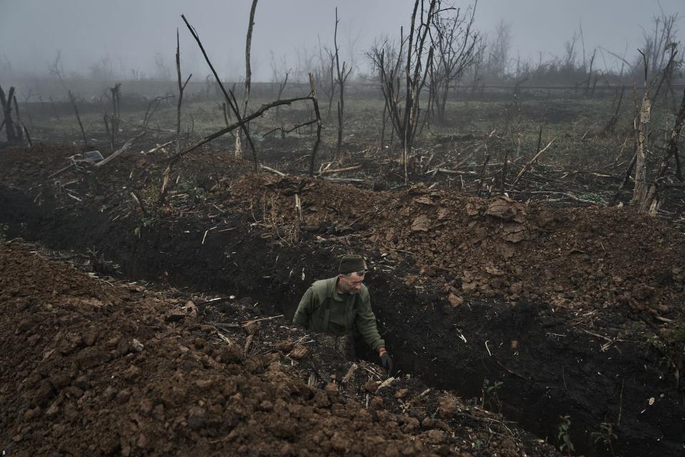 A Ukrainian soldier in a trench surrounded by fog and burnt trees