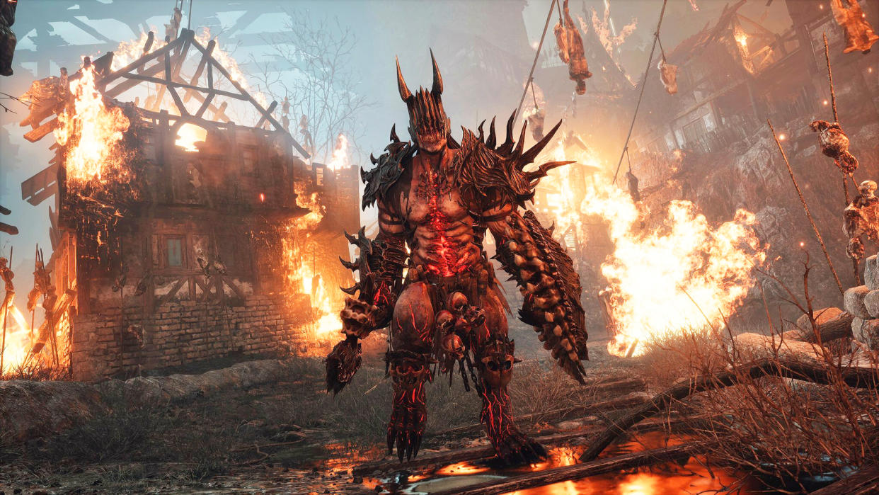  Character in metallic armor with spikes walking away from burning village in Lords of the Fallen. 