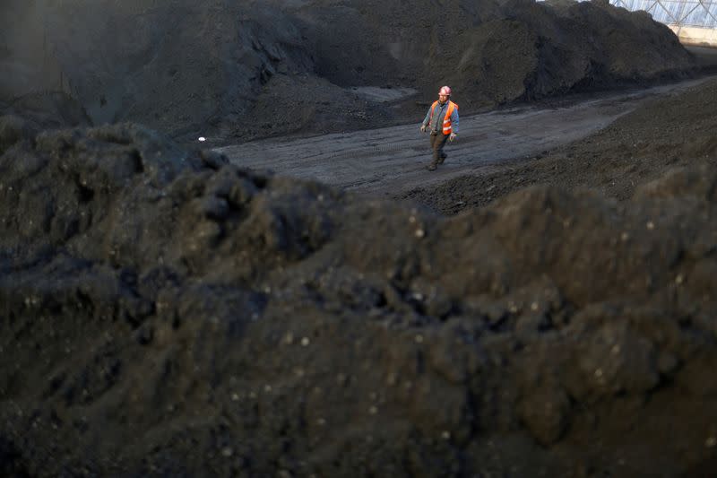 FILE PHOTO: Worker walks past coal piles at a coal coking plant in Yuncheng