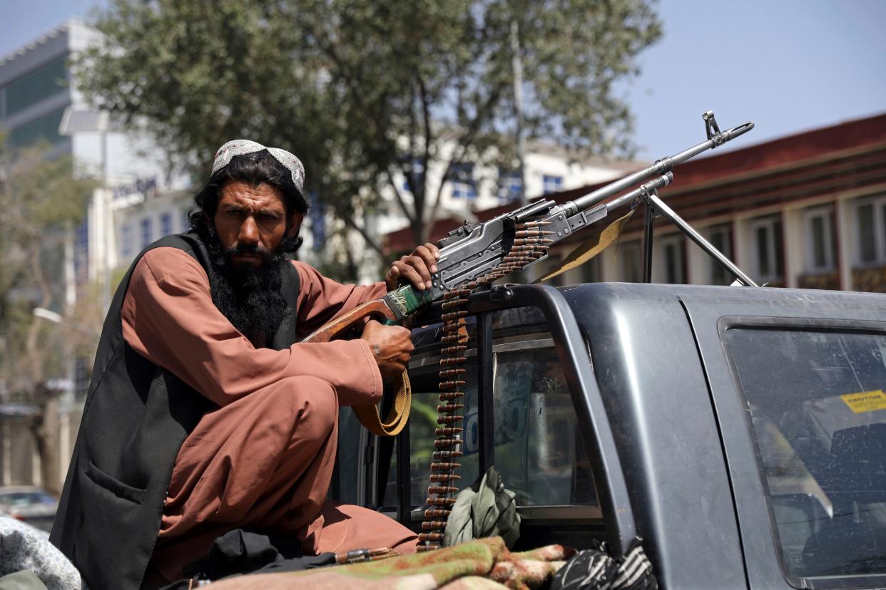 A Taliban fighter sits on the back of a vehicle with a machine gun in front of the main gate leading to the Afghan presidential palace in Kabul, Afghanistan, Monday, Aug. 16, 2021. The U.S. military has taken over Afghanistan's airspace as it struggles to manage a chaotic evacuation after the Taliban rolled into the capital.