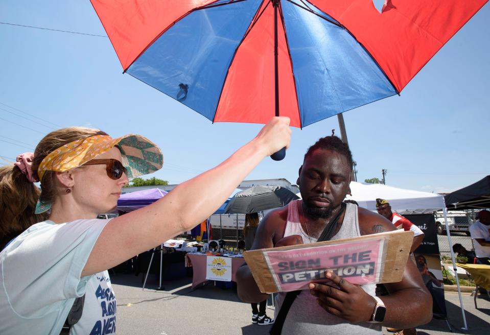 Ellie Hill, left, a volunteer with Arkansans for Limited Government, holds Carl Robinson's umbrella while he signs the petition for the Arkansas abortion amendment during the 15th Annual Juneteenth in Da Rock celebration at S. Arch Street in Little Rock, Ark., Saturday, June 15, 2024.