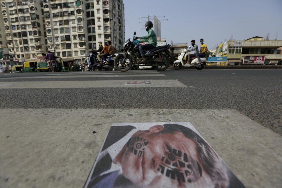 Indian commuters move on defaced images of French President Emmanuel Macron pasted by protestors on a road in Ahmedabad, India, Sunday, Nov. 1, 2020. Muslims have been calling for both protests and a boycott of French goods in response to France's stance on caricatures of Islam's most revered prophet. (AP Photo/Ajit Solanki)