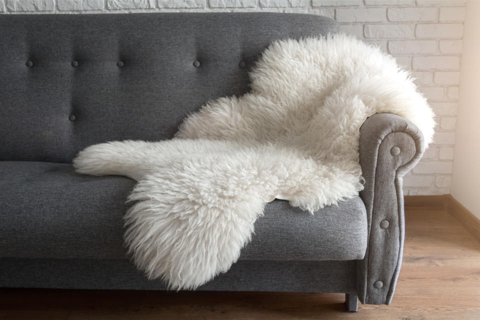 White faux animal hide rug draped over a gray couch.