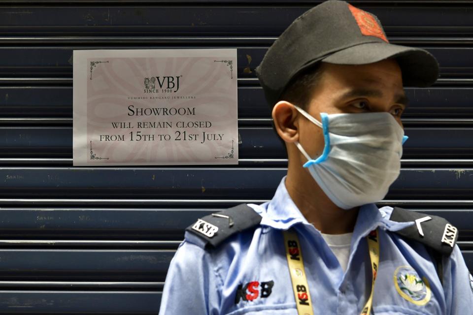 A security guard stands outside a closed jewelry store next to a sign informing customers of a weeklong closure as Bengaluru undergoes a lockdown to contain the surge of coronavirus cases, July 14, 2020. (Photo: MANJUNATH KIRAN via Getty Images)