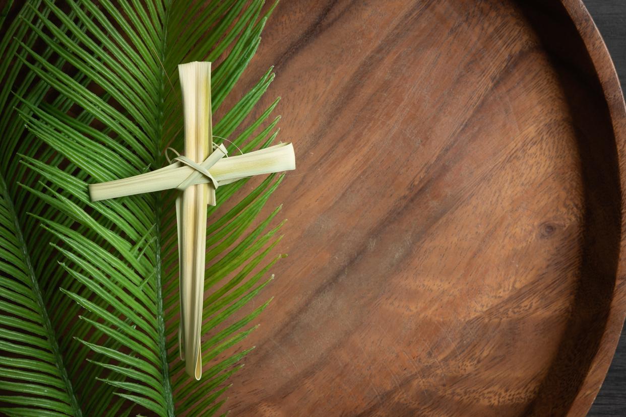 Border of cross made from dried palm leaf laying on a palm branch.