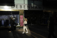 A woman wearing a face mask walks past the Debenhams flagship department store on Oxford Street, during England's second coronavirus lockdown in London, Tuesday, Dec. 1, 2020. In another dark day for the British retailing industry, Debenhams said Tuesday it will start liquidating its business after a potential buyer of the company pulled out, a move that looks like it will cost 12,000 workers their jobs. (AP Photo/Matt Dunham)