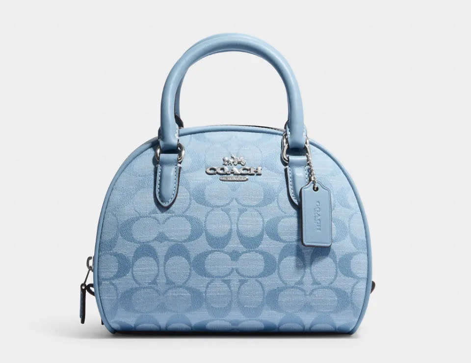 Bolso satchel Sydney en batista con el monograma de la marca. Imagen vía Coach Outlet.