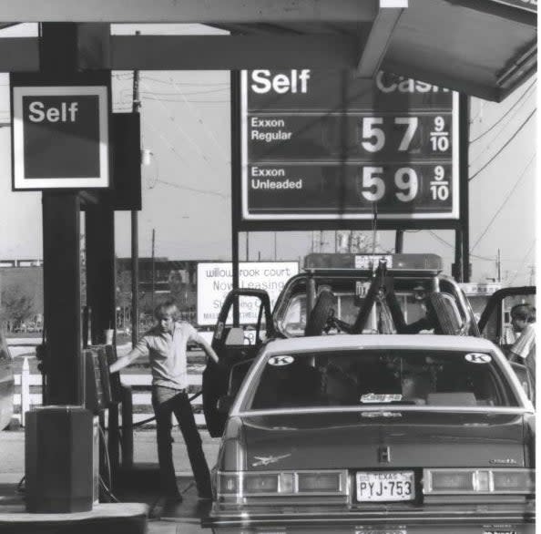 Old gas station with high fuel prices, car at pump and person in background