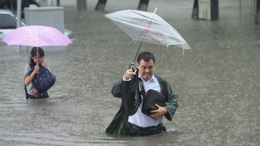 People hold umbrellas as they walk past a flooded street in Taiyuan, Shanxi Province, China, July 19, 2016.