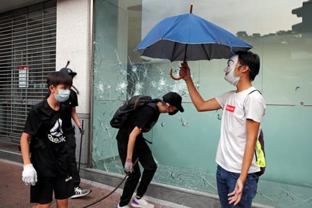 Anti-government protesters wearing masks walk past a damaged bureau of Bank of China during a demonstration at Mong Kok in Hong Kong