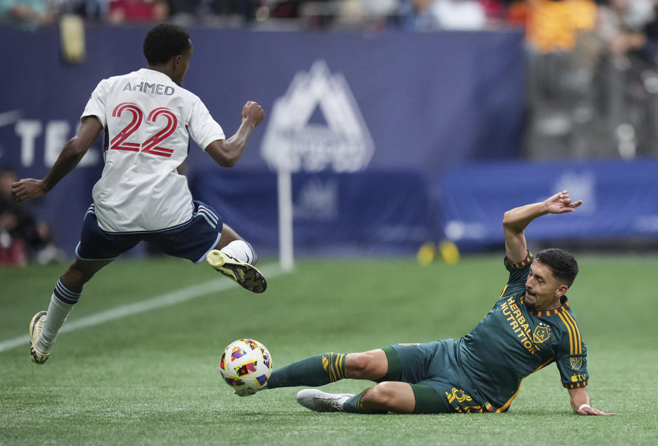 LA Galaxy's Mark Delgado, right, slides to take the ball away from Vancouver Whitecaps' Ali Ahmed during the first half of an MLS soccer match Saturday, April 13, 2024, in Vancouver, British Columbia. (Darryl Dyck/The Canadian Press via AP)