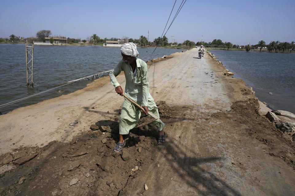 A worker repairs a dusty road surrounded by remaining water of last year's floods, near Therhi town in Khairpur, a district of Pakistan's Sindh province, Saturday, May 20, 2023. A year on from the floods in Pakistan that killed at least 1,700 people, destroyed millions of homes, wiped out swathes of farmland, and caused billions of dollars in economic losses, the country still hasn't fully recovered. (AP Photo/Anjum Naveed)