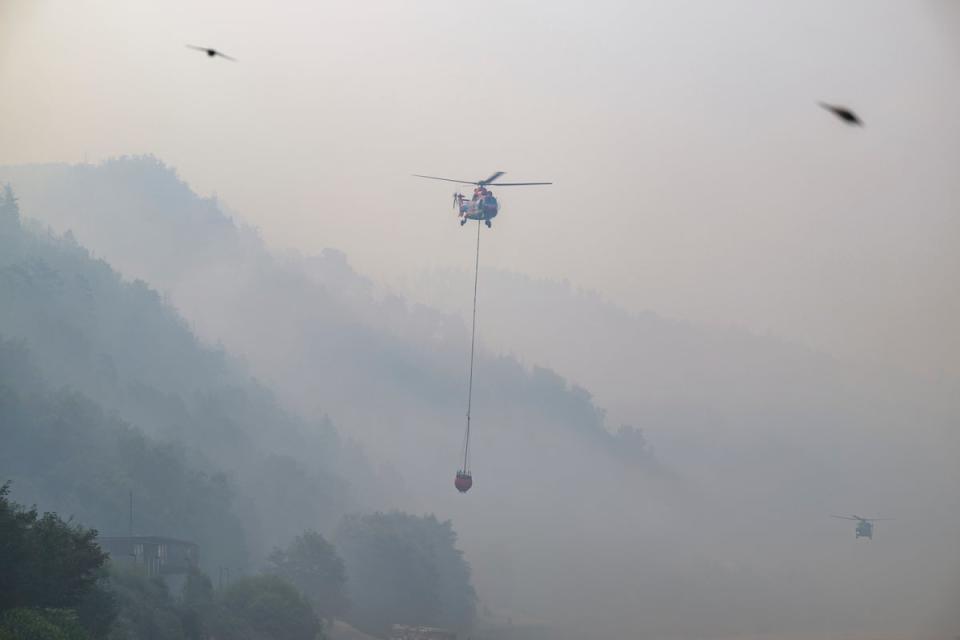 A cargo helicopter from Austria takes water from the Elbe River with an external water tank to extinguish a fire (Robert Michael/dpa via AP)