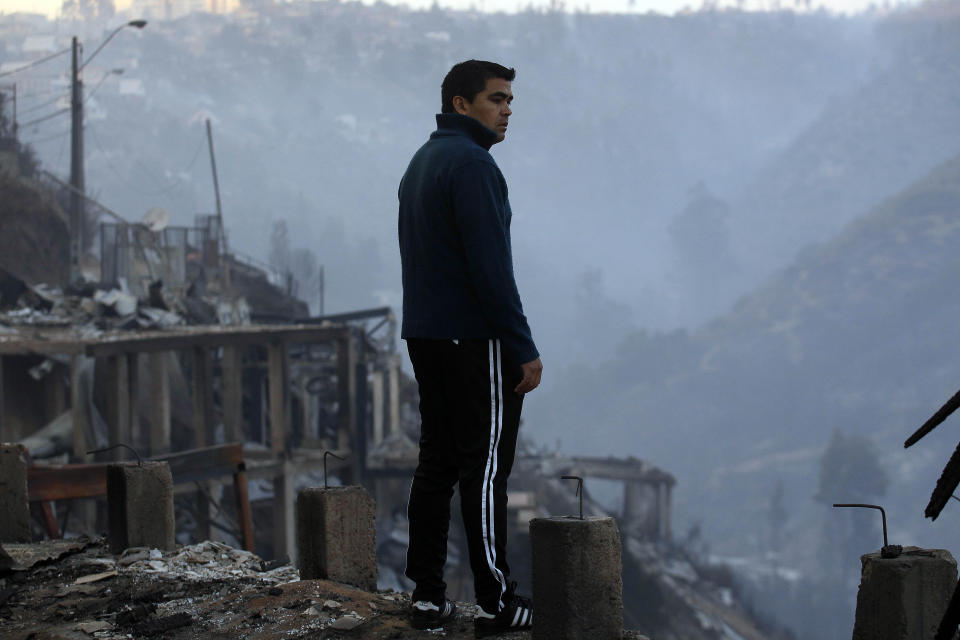 A man looks at the charred remains of homes after a large forest fire reached urban areas in Valparaiso, Chile, Sunday April 13, 2014. Authorities say the fires have destroyed hundreds of homes, forced the evacuation of thousands and claimed the lives of at least seven people. ( AP Photo/ Luis Hidalgo)