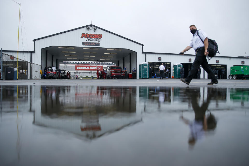 A man is reflected in a rain puddle as he walks near the Cup cars garages before the scheduled NASCAR Truck Series auto race at Pocono Raceway, Saturday, June 27, 2020, in Long Pond, Pa. (AP Photo/Matt Slocum)